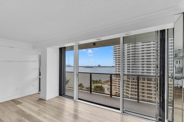 empty room featuring expansive windows, a water view, baseboards, and wood finished floors