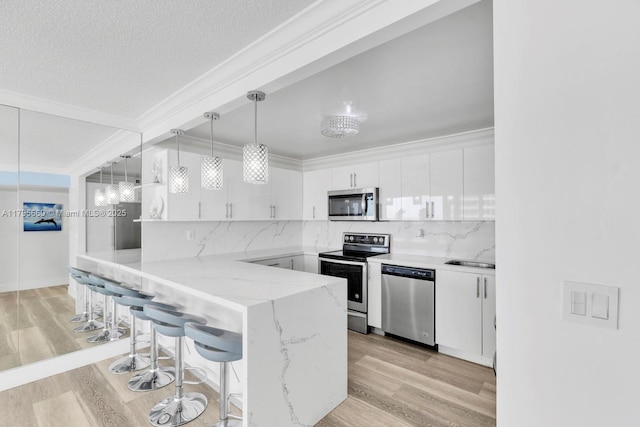 kitchen featuring a breakfast bar area, crown molding, white cabinets, a peninsula, and stainless steel appliances