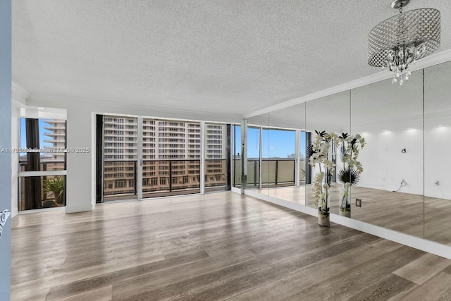 unfurnished living room featuring crown molding, a textured ceiling, wood finished floors, and a notable chandelier