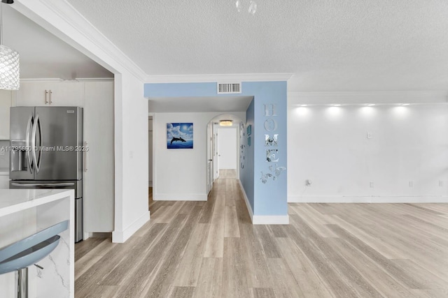 interior space featuring a textured ceiling, visible vents, light wood finished floors, stainless steel fridge, and ornamental molding