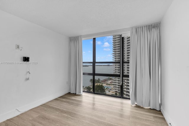 empty room with expansive windows, a water view, wood finished floors, and a wealth of natural light