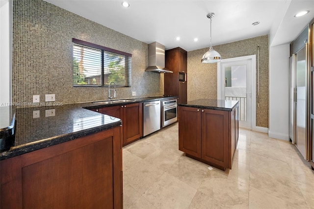kitchen featuring wall chimney range hood, appliances with stainless steel finishes, a sink, a center island, and decorative backsplash
