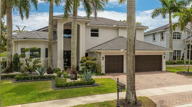 mediterranean / spanish house featuring a garage, a front yard, decorative driveway, stucco siding, and a tiled roof