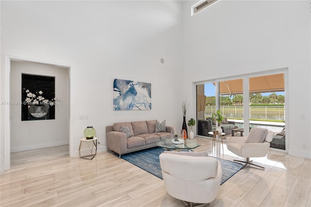 living room featuring baseboards, visible vents, light wood-style flooring, and a towering ceiling