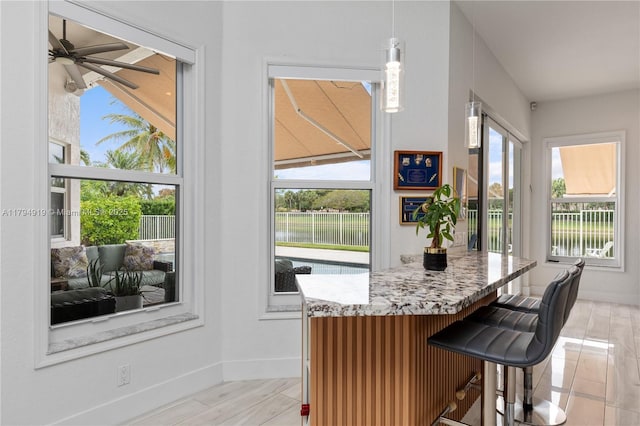 kitchen featuring hanging light fixtures, a ceiling fan, baseboards, a kitchen bar, and a water view