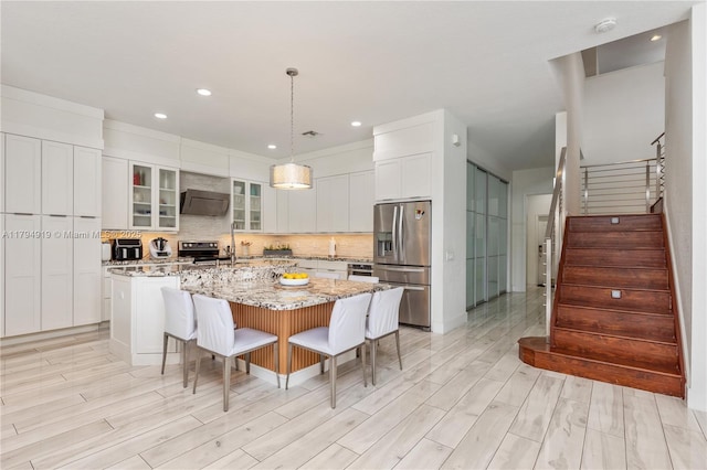 kitchen with a kitchen island with sink, a breakfast bar area, white cabinets, tasteful backsplash, and appliances with stainless steel finishes