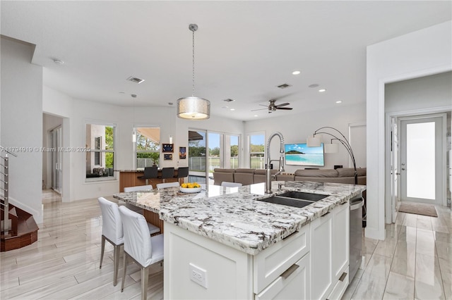 kitchen featuring light stone countertops, a center island with sink, a sink, open floor plan, and recessed lighting