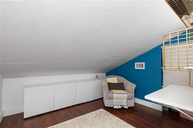 interior space featuring visible vents, wood finished floors, baseboards, a textured ceiling, and vaulted ceiling