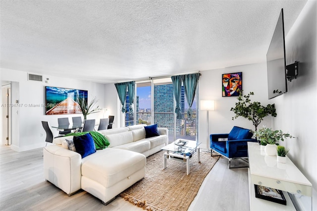 living room featuring a wall of windows, a textured ceiling, visible vents, light wood-type flooring, and baseboards