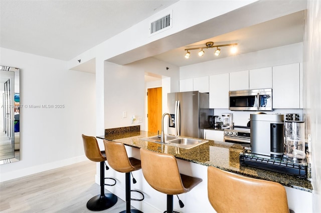 kitchen featuring appliances with stainless steel finishes, a sink, dark stone countertops, a peninsula, and visible vents