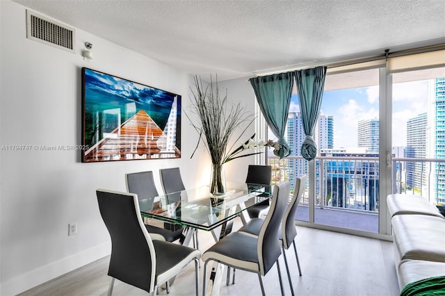 dining space featuring a textured ceiling, baseboards, wood finished floors, visible vents, and a city view
