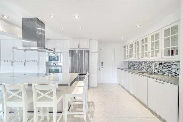 kitchen with white cabinetry, tasteful backsplash, island exhaust hood, a sink, and appliances with stainless steel finishes