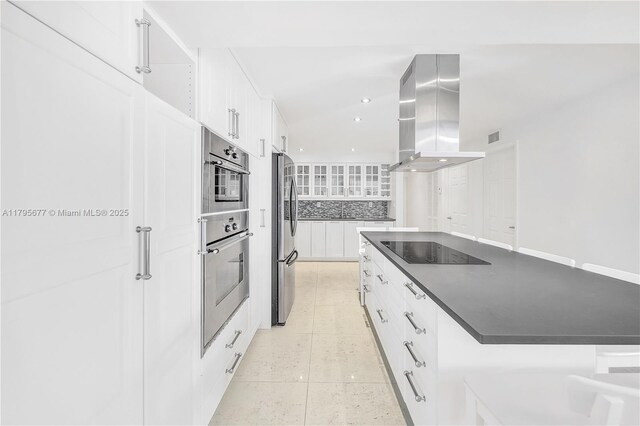 kitchen featuring backsplash, island range hood, dark countertops, appliances with stainless steel finishes, and white cabinets