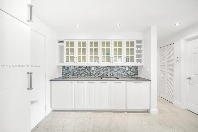 kitchen featuring backsplash, white cabinets, glass insert cabinets, and a sink