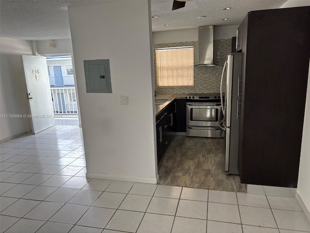 kitchen with wall chimney range hood, a textured ceiling, stainless steel appliances, light tile patterned floors, and electric panel