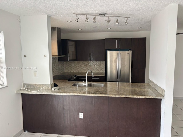 kitchen with a sink, freestanding refrigerator, a peninsula, and wall chimney exhaust hood