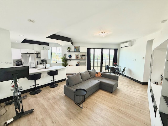 living area featuring light wood-style floors, baseboards, and a wall unit AC
