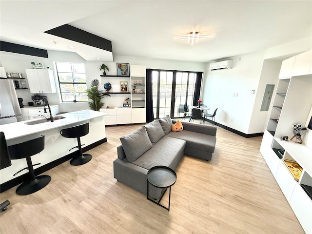 living area featuring baseboards, an AC wall unit, and light wood-style flooring