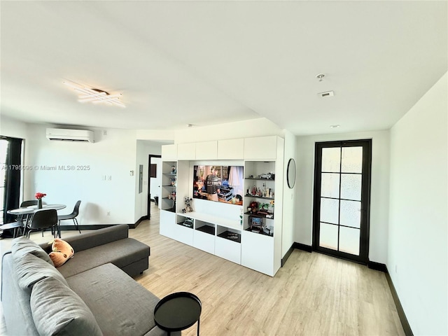 living area featuring an AC wall unit, light wood finished floors, and baseboards