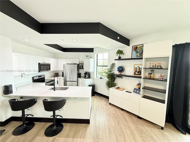 kitchen featuring a peninsula, light wood-style floors, white cabinetry, a sink, and appliances with stainless steel finishes