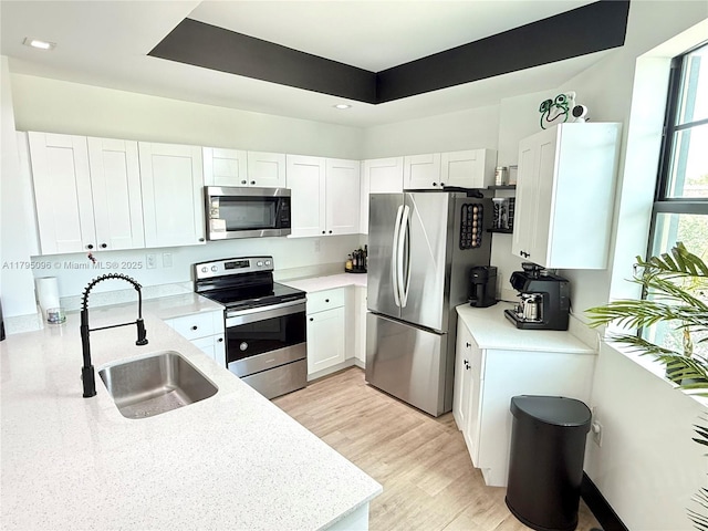 kitchen with a raised ceiling, white cabinets, a sink, light wood finished floors, and appliances with stainless steel finishes