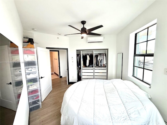 bedroom with ceiling fan, a wall mounted AC, wood finished floors, and a closet