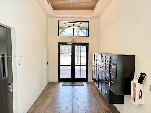 entrance foyer featuring wood finished floors, baseboards, mail area, a tray ceiling, and french doors