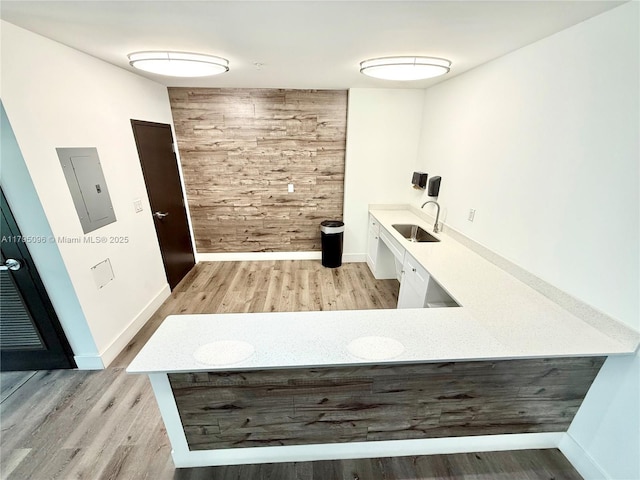 unfurnished office with a sink, baseboards, electric panel, and light wood-style flooring