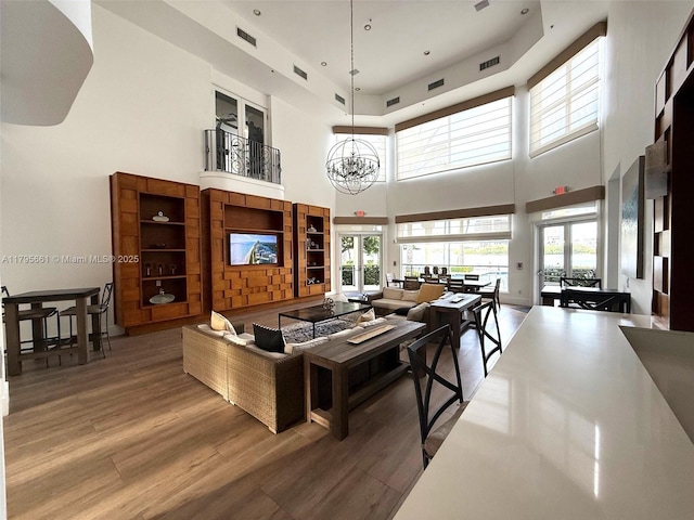 living room with a towering ceiling, visible vents, wood finished floors, and a chandelier