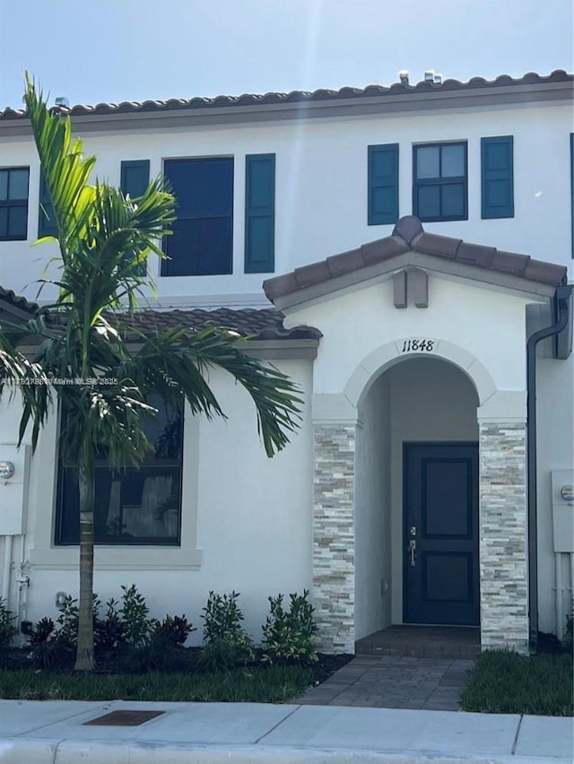 entrance to property featuring stucco siding, a tile roof, and stone siding