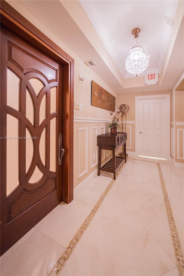 foyer with a decorative wall, a chandelier, a wainscoted wall, a tray ceiling, and visible vents