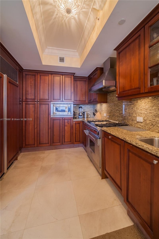 kitchen with wall chimney range hood, decorative backsplash, visible vents, a raised ceiling, and stainless steel appliances