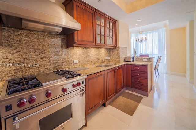 kitchen with light stone counters, a sink, a chandelier, wall chimney exhaust hood, and premium stove