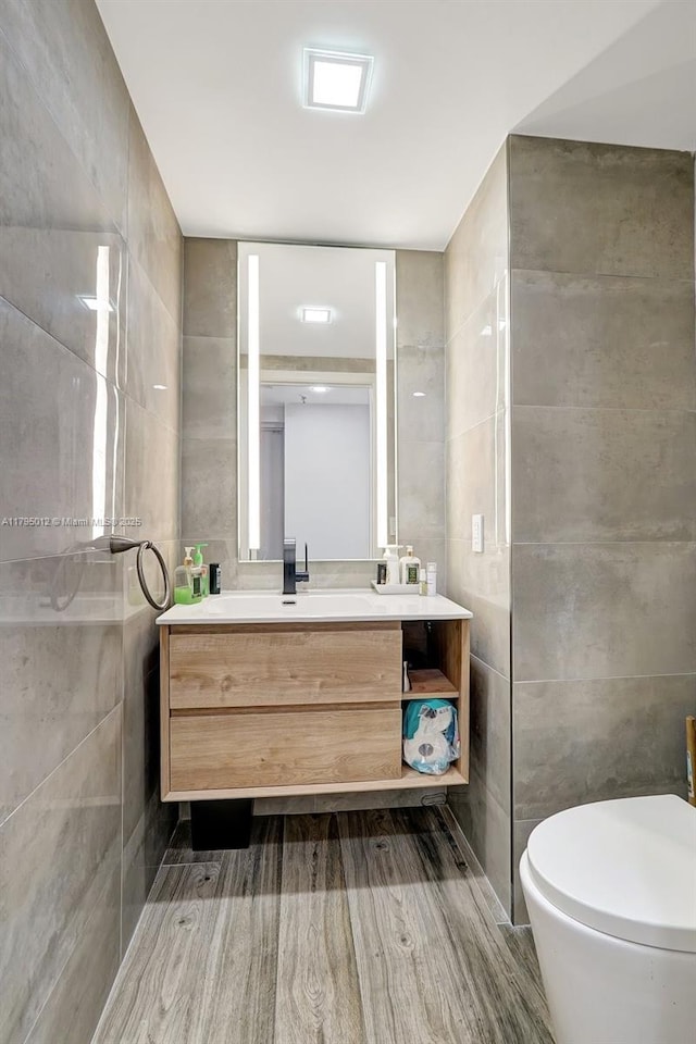 bathroom with tile walls, vanity, toilet, and wood finished floors