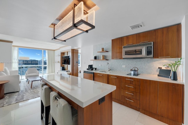 6801 Collins Ave Unit 702, Miami Beach, FL 33141 - kitchen with stainless steel microwave, a sink, brown cabinetry, open floor plan, and light tile patterned flooring