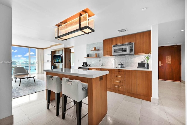 kitchen featuring visible vents, open shelves, a center island, stainless steel microwave, and brown cabinets