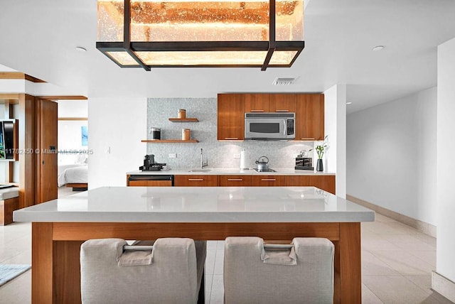 kitchen with visible vents, modern cabinets, brown cabinets, light countertops, and stainless steel microwave
