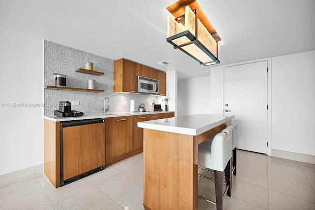 kitchen with brown cabinetry, open shelves, light tile patterned flooring, light countertops, and stainless steel microwave