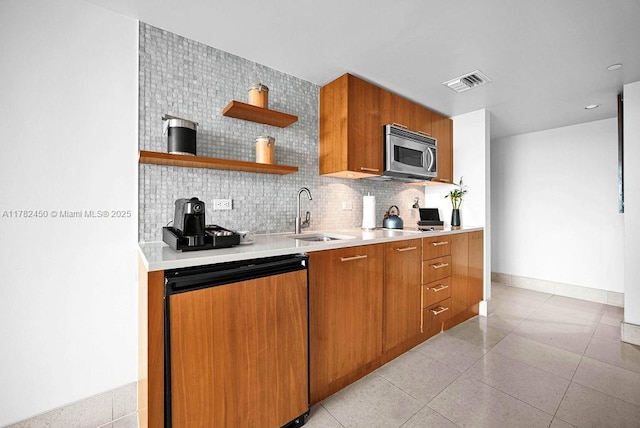 kitchen featuring visible vents, brown cabinetry, light countertops, stainless steel microwave, and a sink