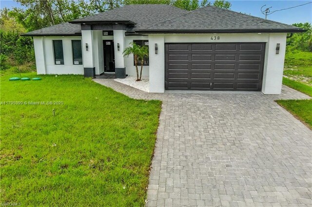 prairie-style home with a front yard, roof with shingles, decorative driveway, an attached garage, and stucco siding