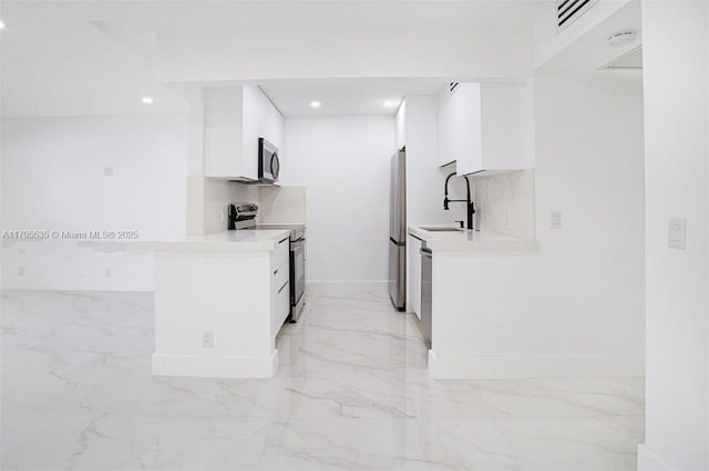 kitchen with white cabinets, appliances with stainless steel finishes, a sink, marble finish floor, and baseboards