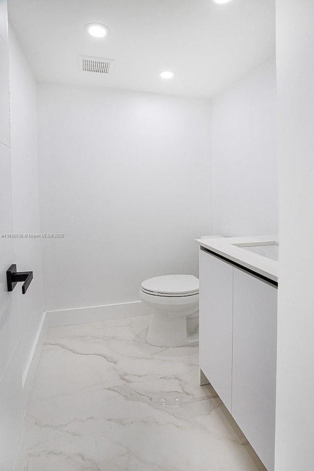 half bath with visible vents, vanity, toilet, marble finish floor, and recessed lighting