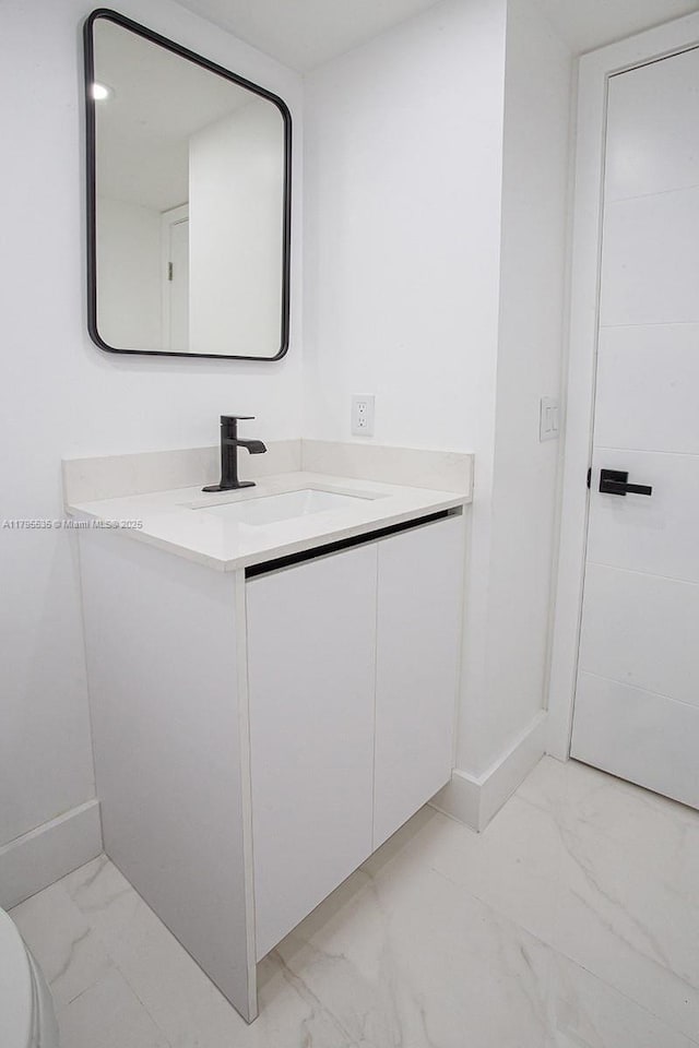 half bath with vanity, marble finish floor, and baseboards