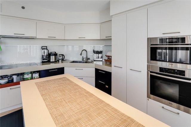 kitchen featuring white cabinets, stainless steel double oven, a sink, light countertops, and backsplash
