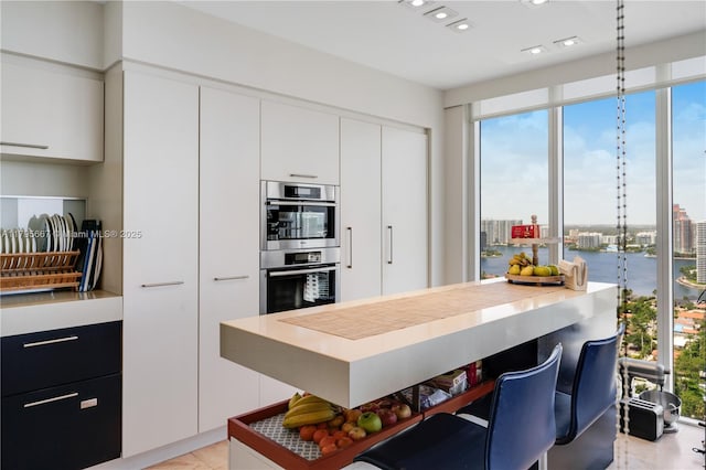kitchen featuring double oven, modern cabinets, white cabinetry, light tile patterned floors, and decorative light fixtures