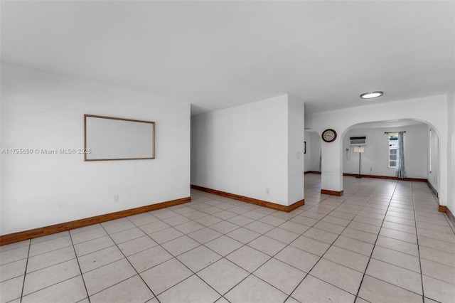 empty room featuring arched walkways, baseboards, and light tile patterned flooring
