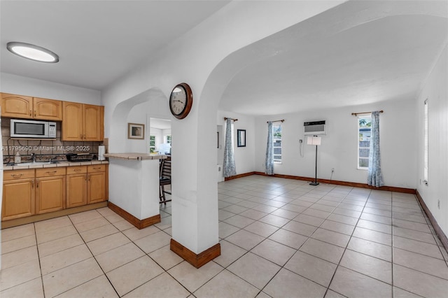 kitchen with arched walkways, decorative backsplash, stainless steel microwave, and light tile patterned flooring