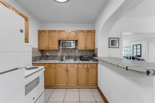 kitchen featuring white appliances, tile counters, tasteful backsplash, a sink, and light tile patterned floors