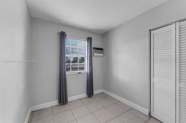 unfurnished bedroom with a closet, a wall mounted air conditioner, baseboards, and light tile patterned floors
