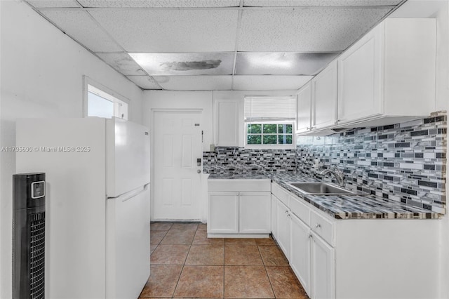 kitchen featuring decorative backsplash, freestanding refrigerator, a drop ceiling, white cabinets, and a sink